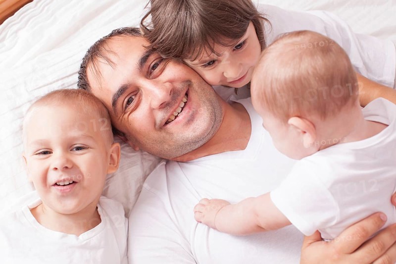The father with three children in white laughing and playing on the bed