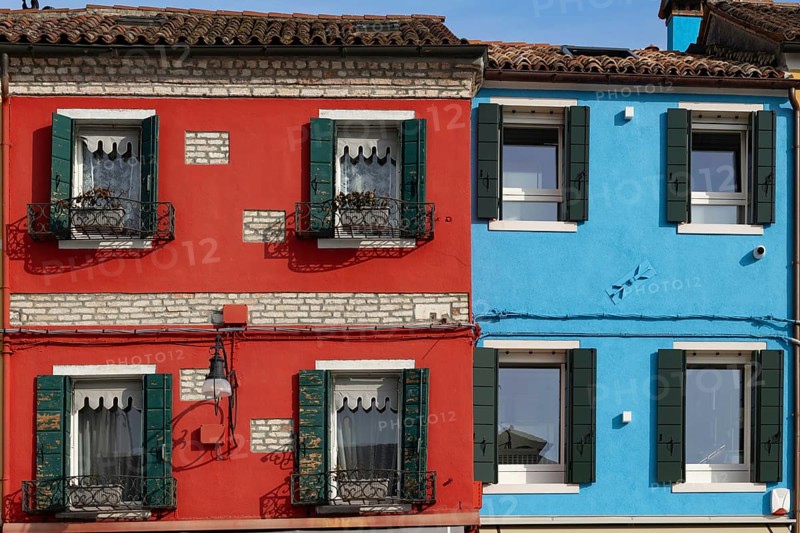 Close-up of red and blue houses with classic shutters and rustic façade, Burano, Venice, Veneto region, Italy