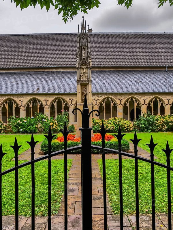 Iron gate in front of a garden in the monastery courtyard with well-tended flowerbeds and Gothic architecture, Xanten, North Rhine-Westphalia, Germany
