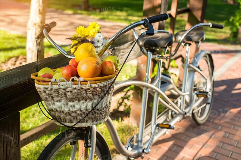 Basket of fruits on bicycle. Bike and bouquet on fence. Organize a picnic for two. Warm days of august