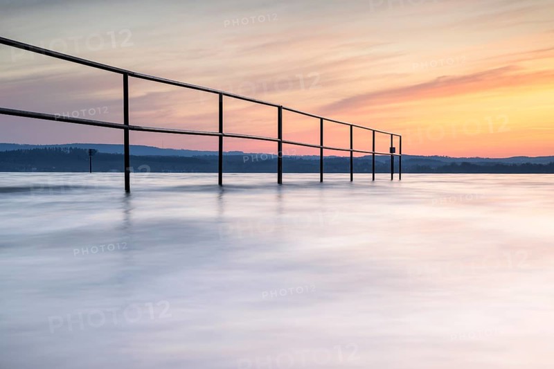 A railing in calm water, surrounded by a pastel-coloured sunrise, lido, Litzelstetten, Lake Constance, Baden-Württemberg, Germany