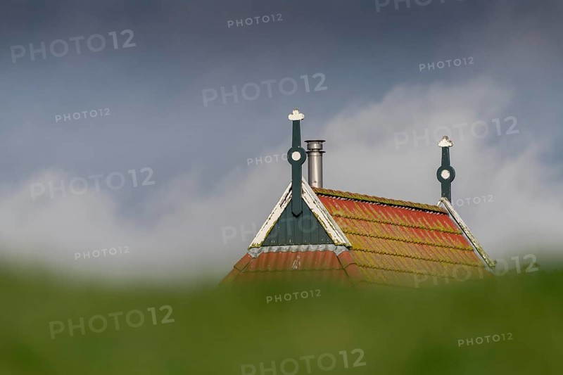 Colorful gable of a farm behind a green dike in northern Netherlands