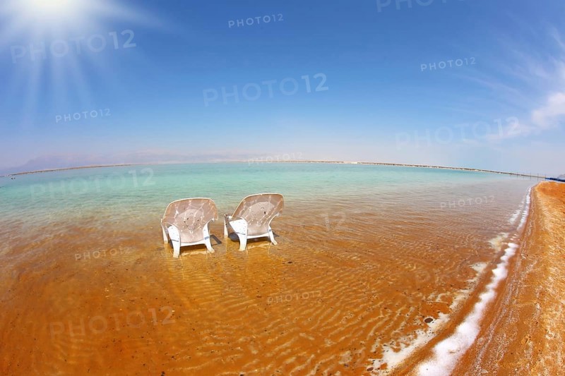 Two white beach chairs stood side by side in the clear water. The sun shines on the beach therapeutic