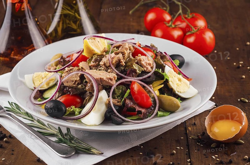 food still-life, Fresh nicoise salad with tuna, eggs, olives, and tomatoes on a wooden table with olive oil and rosemary