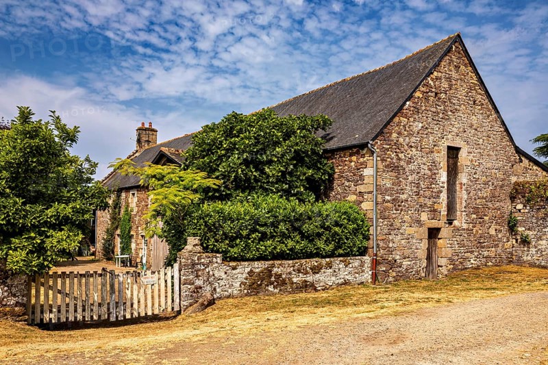 Rural stone house with a small wooden fence and green bushes under a clear sky, The Abbey de La Lucerne in Normandy, France
