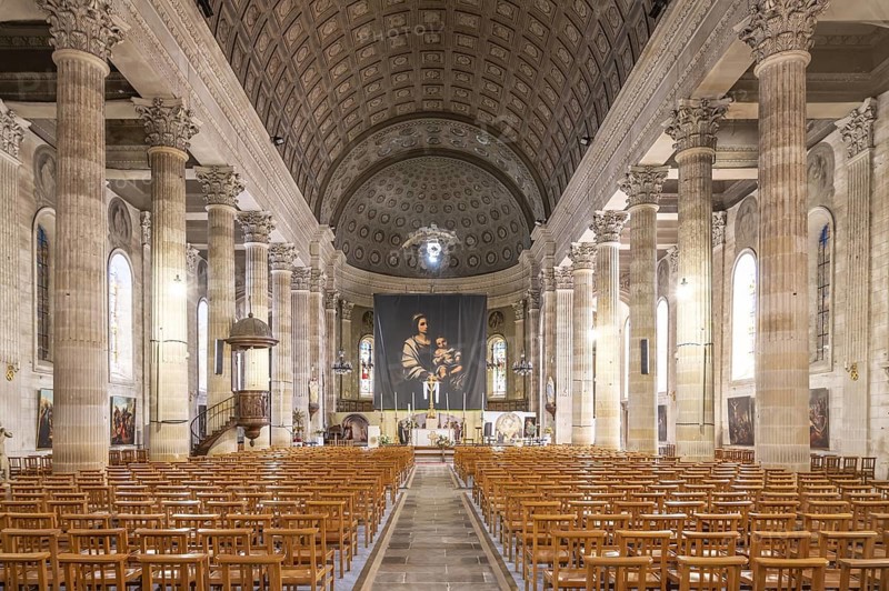 Neoclassical church interior of the Eglise Saint-Louis with monumental columned peristyle of rudentated and fluted Corinthian columns, continuous entablature, imposing wood-panelled barrel vault ceiling with coffered structure and painted rosettes in trompe-l'oeil, flooded with light through Renaissance glazing and Madonna and Child as central altar motif, La Roche sur Yon, Vendee, Pays de la Loire, France
