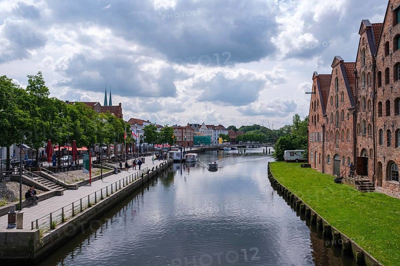City view with waterway and historic brick buildings, flanked by green areas and clouds, Lübeck, Schleswig-Holstein, Germany