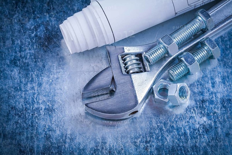 Steel adjustable spanner screw-nuts bolts and blueprints on scratched metallic background construction concept
