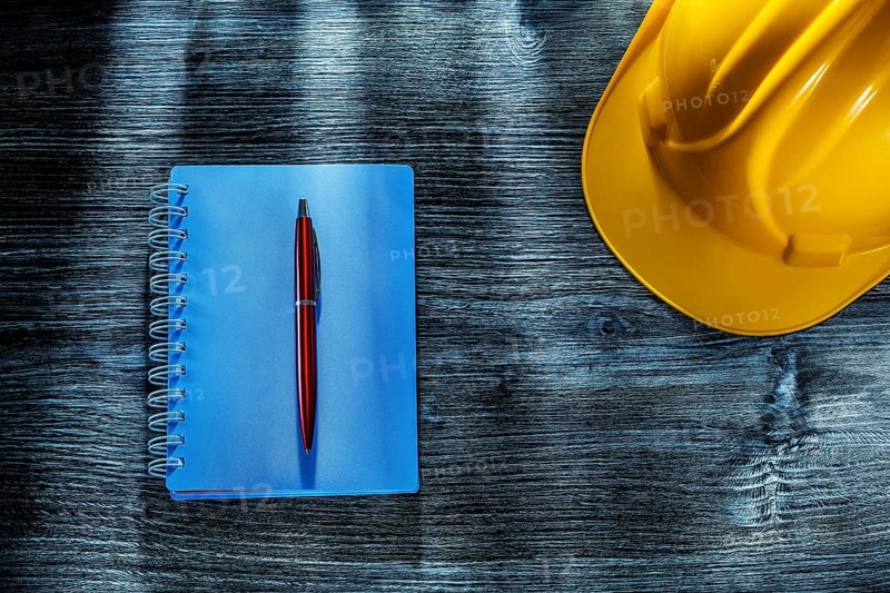 Notepad pen hard hat on wooden board