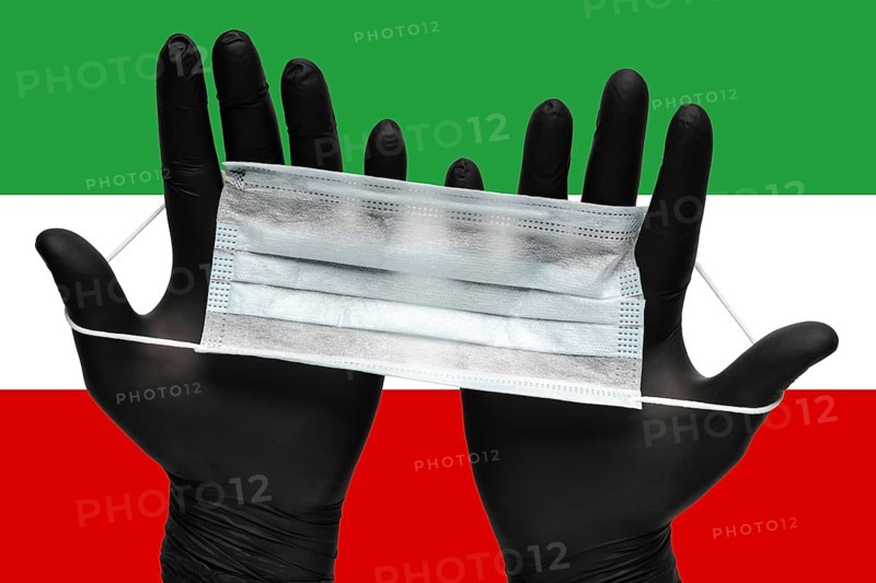 Doctor holds respiratory face mask in hands in black medical gloves on background colors flag of Islamic Republic of Iran. Concept coronavirus quarantine, pandemic outbreak, grippe, airborne diseases