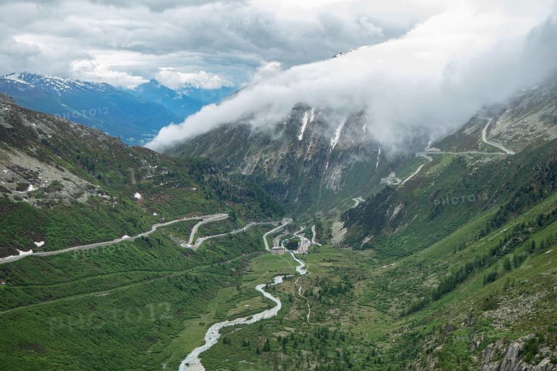 Situation on Furka pass on a cloudy summer day. View into the Rhone valley with mountain passes. Clouds streaming in from the north over Grimsel pass