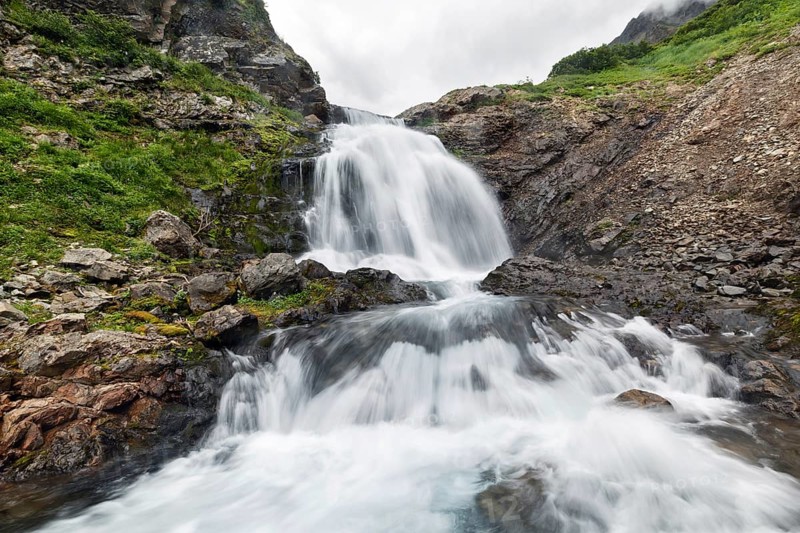 Scenery summer mountain landscape of Kamchatka Peninsula: beautiful view of cascade of flowing stormy water in waterfall in Mountain Range Vachkazhets. Eurasia, Russian Far East, Kamchatka Region