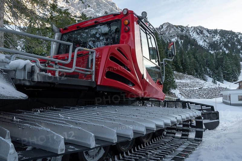 Tracked snow groomer with huge tracks in a winter scenery with the snowy austrian alps and forest in background