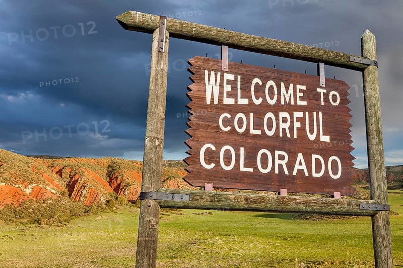 Welcome to colorful Colorado roadside wooden sign with red sandstone cliff in background