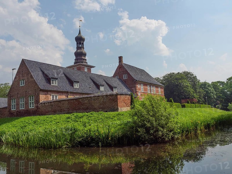 Historic brick building with tower and pond, surrounded by a green garden and blue sky, husum, schleswig-holstein, germany