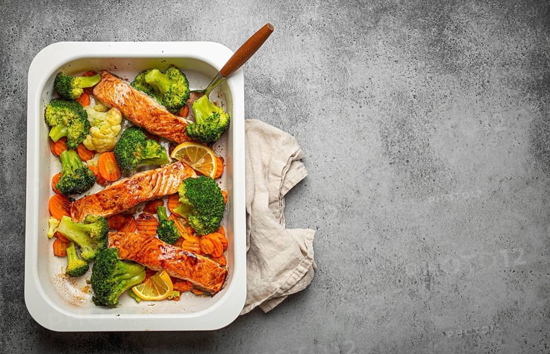 Top view of healthy baked fish salmon steaks, broccoli, cauliflower, carrot in casserole dish on gray stone background. Cooking a delicious low carb dinner, healthy nutrition concept. Space for text, food photography, food photography
