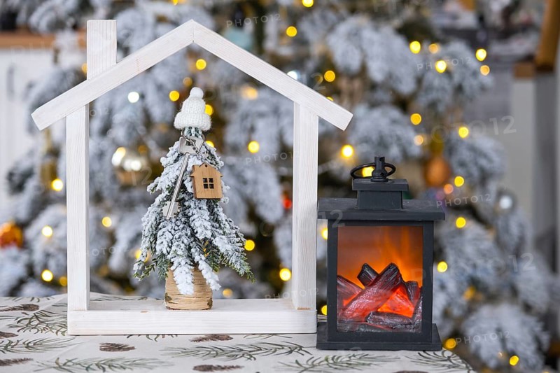 Key on Christmas tree and tiny house on cozy home with Christmas decor on table of festive white kitchen. Gift for New Year. Insurance, moving to new house, mortgage, rent and real estate