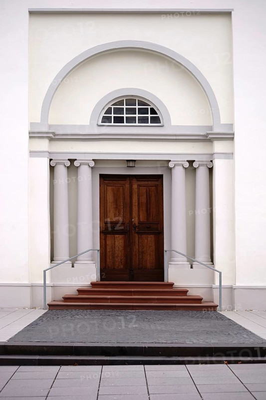 The entrance of a newly built and modern church with an entrance door with a round arch and white walls