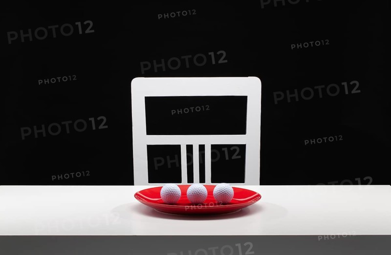 Three white golf balls on the red plate. White old chair and white table in the dark room