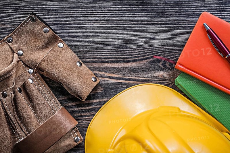 Leather building belt note-books pen yellow hard hat on wooden board top view construction concept