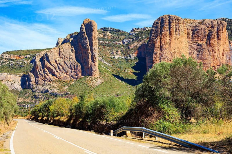 Asphalt highway passes through the rocks. Part of the foothills of the Pyrenees. The Mallets of Riglos. Hot sunny afternoon. Romantic trip to Spain. Hoya de Huesca, Aragon