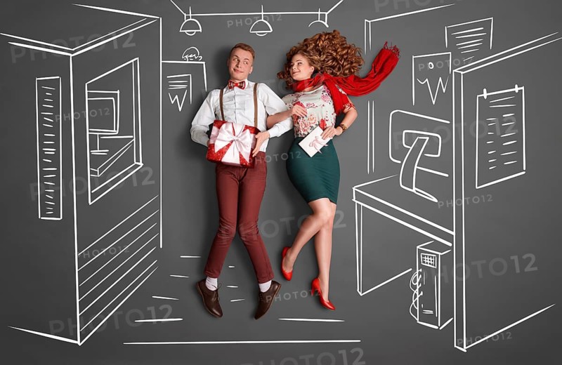 Happy valentines love story concept of an office romance. Young couple at work smiling at each other and exchanging gifts against chalk drawings office background