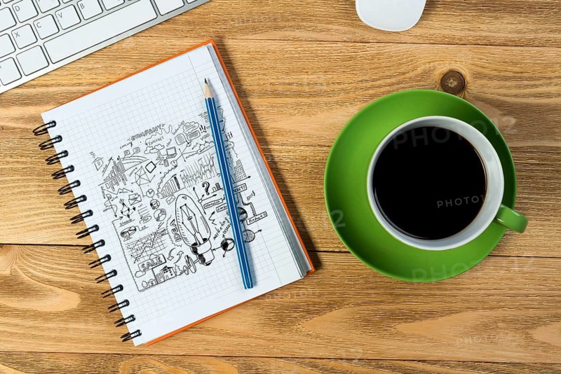 Notepad with idea sketches coffee cup keyboard and pencil on wooden table