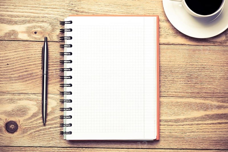 White blank notepad with cup of coffee on wooden table