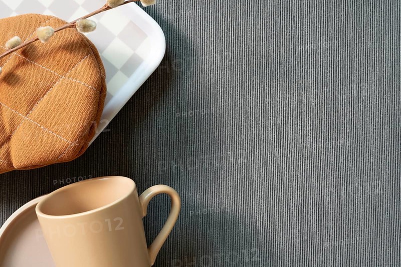 Kitchenware mug cup, dish, gloves, tray on gray fabric background. top view, copy space