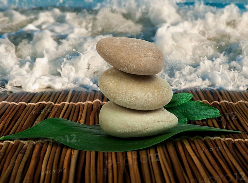 Stacked stones on wooden base for spa and green leafs. Waves on the background
