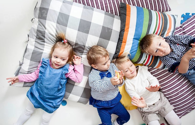 Cute little boys and girls lying on the pillows and playing in the kindergarten, top view