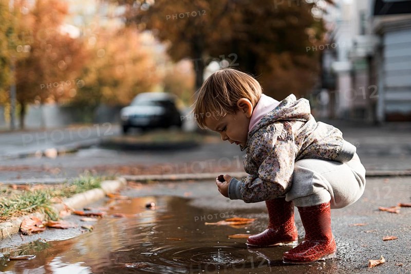 Little girl in red rainboots playing in puddle after rain. Happy fall childhood activity