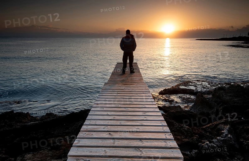 Person standing at the edge of a wooden pier in the sea at sunrise, People active outdoors enjoy ocean. Protaras Cyprus