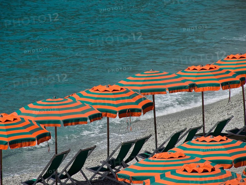 Row of striped parasols on a pebbly beach with a view of the sea and gentle waves, Monte rosso, cinque terre, Italy