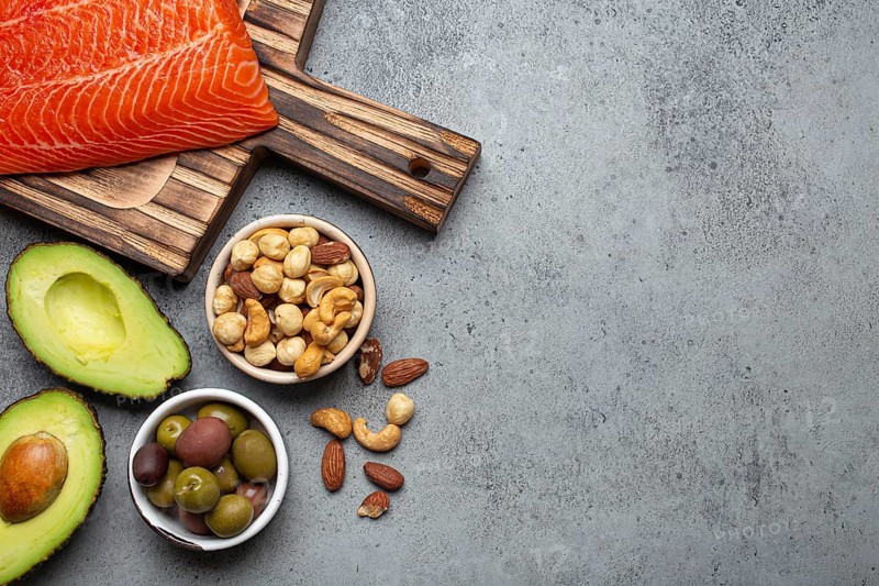 Food sources of healthy unsaturated fat and omega 3: fresh raw salmon fillet, avocado, olives, nuts on cutting board, rustic stone background top view. Healthy nutrition and keto diet, space for text, food photography, food photography