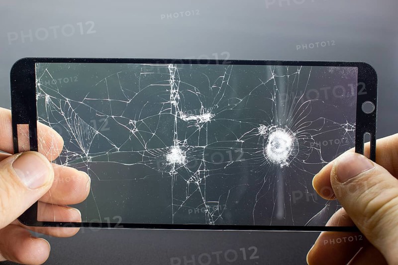 Broken protective glass of smartphone with cracks in hands on black background. Damaged protective glass, photo while replacing screen protector, cellphone repair