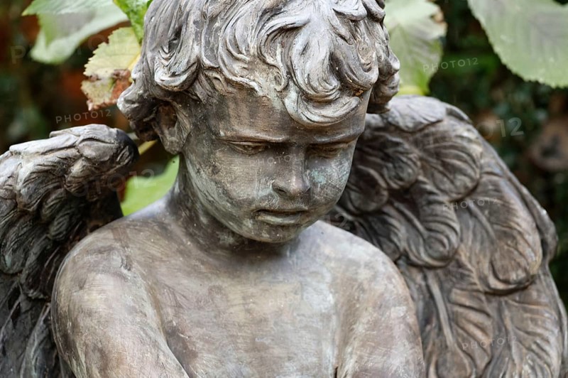Little angel in a cemetery looks sadly to the ground