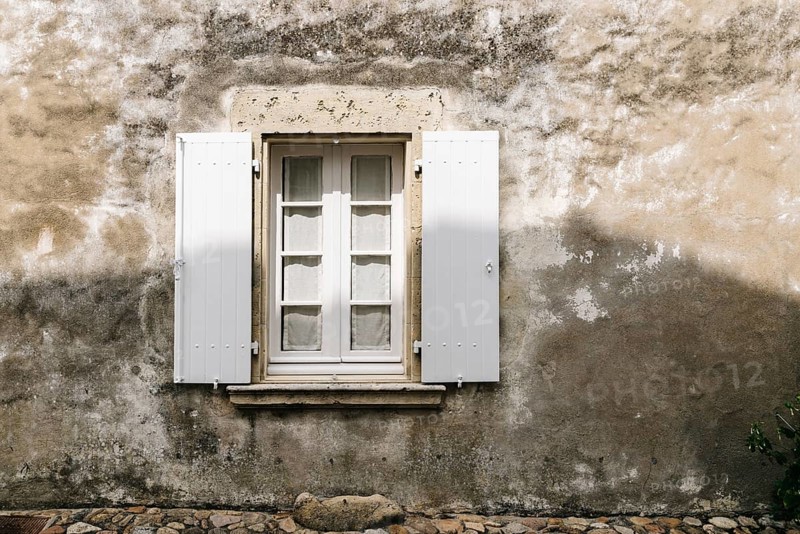 Old window with wooden white painted open shutters in weathered plaster wall