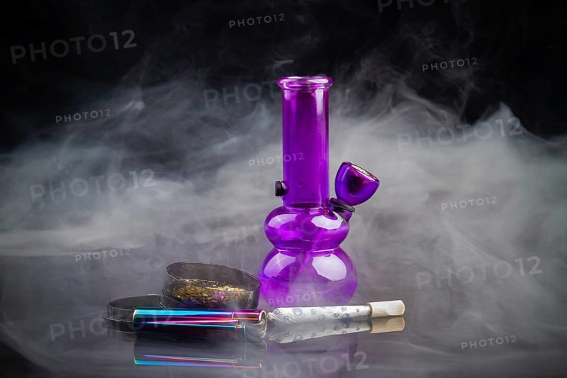 Purple glass bong pipe with joint and a lot of smoke. Cannabis smoker starter pack