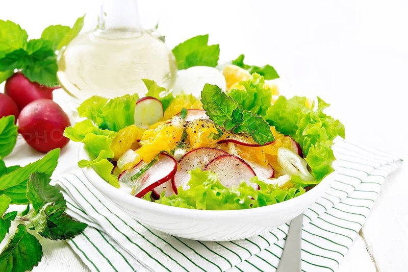 Radish, onion and orange salad with mint, vegetable oil and spices on lettuce in a plate on a towel on white wooden board backgroun