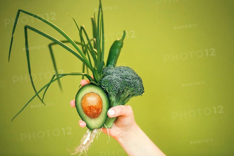 Unrecognizable female demonstrating bunch of healthy fresh vegetables while being on diet against green background