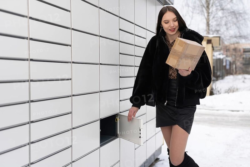 An attractive student collects and sends a parcel via a parcel locker in winter. Automatic machine for sending and receiving letters and parcels