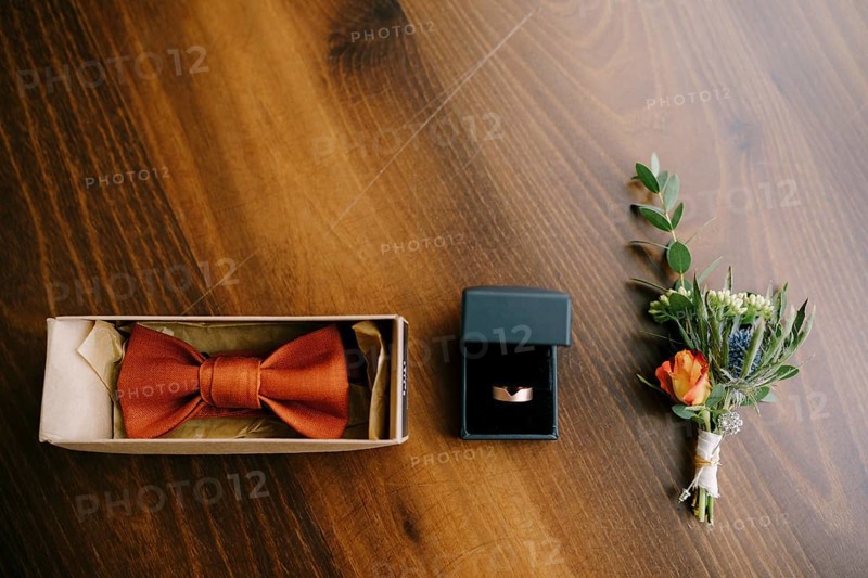 Accessories for the groom bow tie, gold wedding ring and boutonniere on a wooden floor in a row.