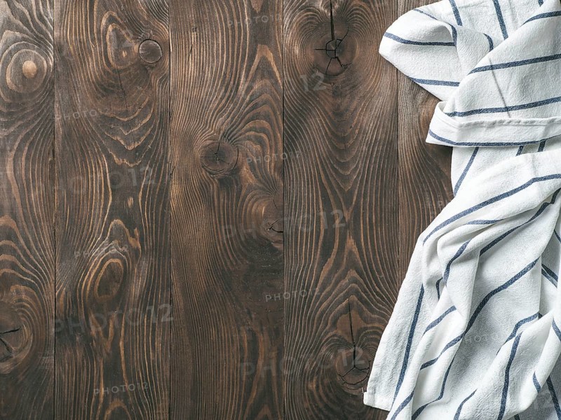 View from above on brown wooden table with linen kitchen towel or textile napkin. Blue tablecloth on dark brown wood tabletop. Copy space for text. Can use as mock up for design