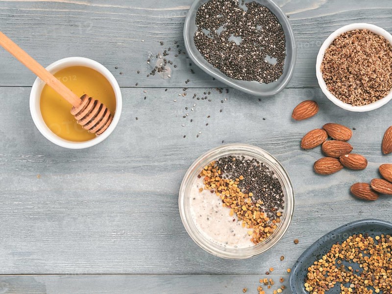 Overnight oats in jar and ingredients - chia seeds, almond, LSA, honey and pollen on gray wooden table background. Healthy breakfast oatmeal recipe idea. Top view