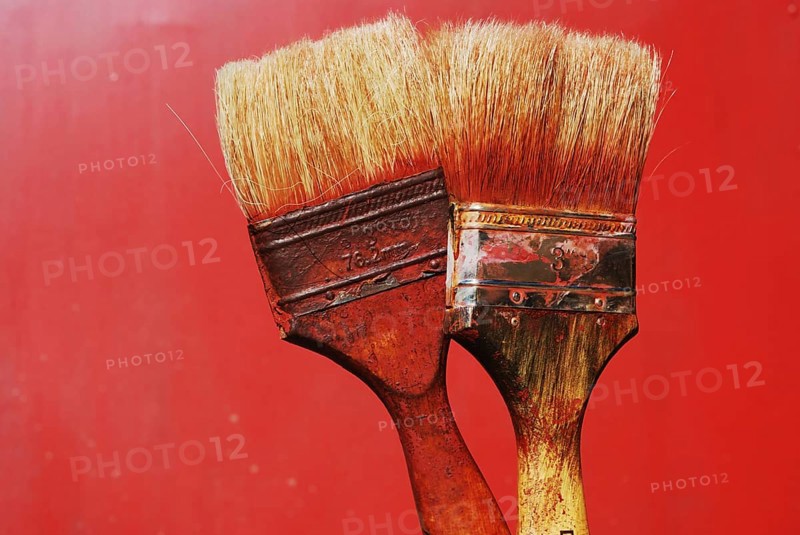 Closeup of two dirty paintbrushes against red background