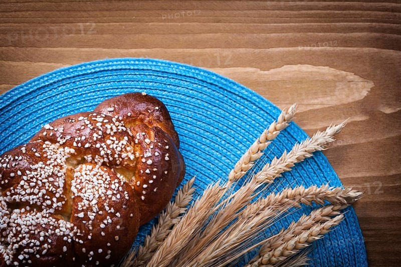 Sweet roll wheat rye ears with blue wattled cover on wooden board food and drink concept