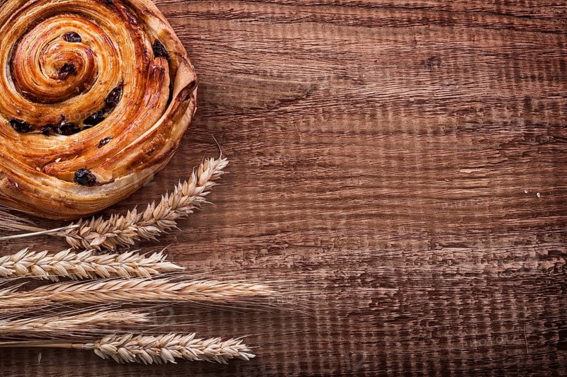 Rich raisin bun bunch of wheat ears on oak wooden board food and drink concept
