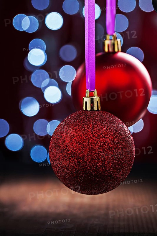 Two red christmas balls hanging on pink tape on old wooden table and blurred bokeh background