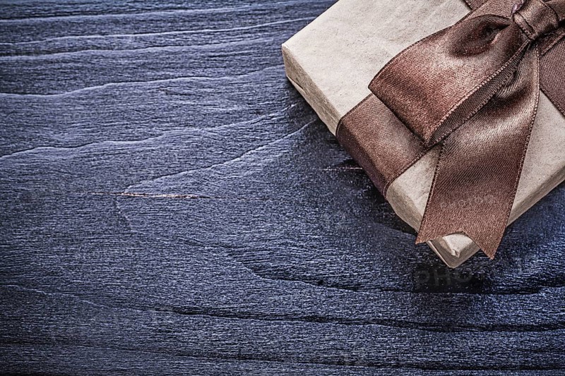Gift box with brown satin bow on wooden board